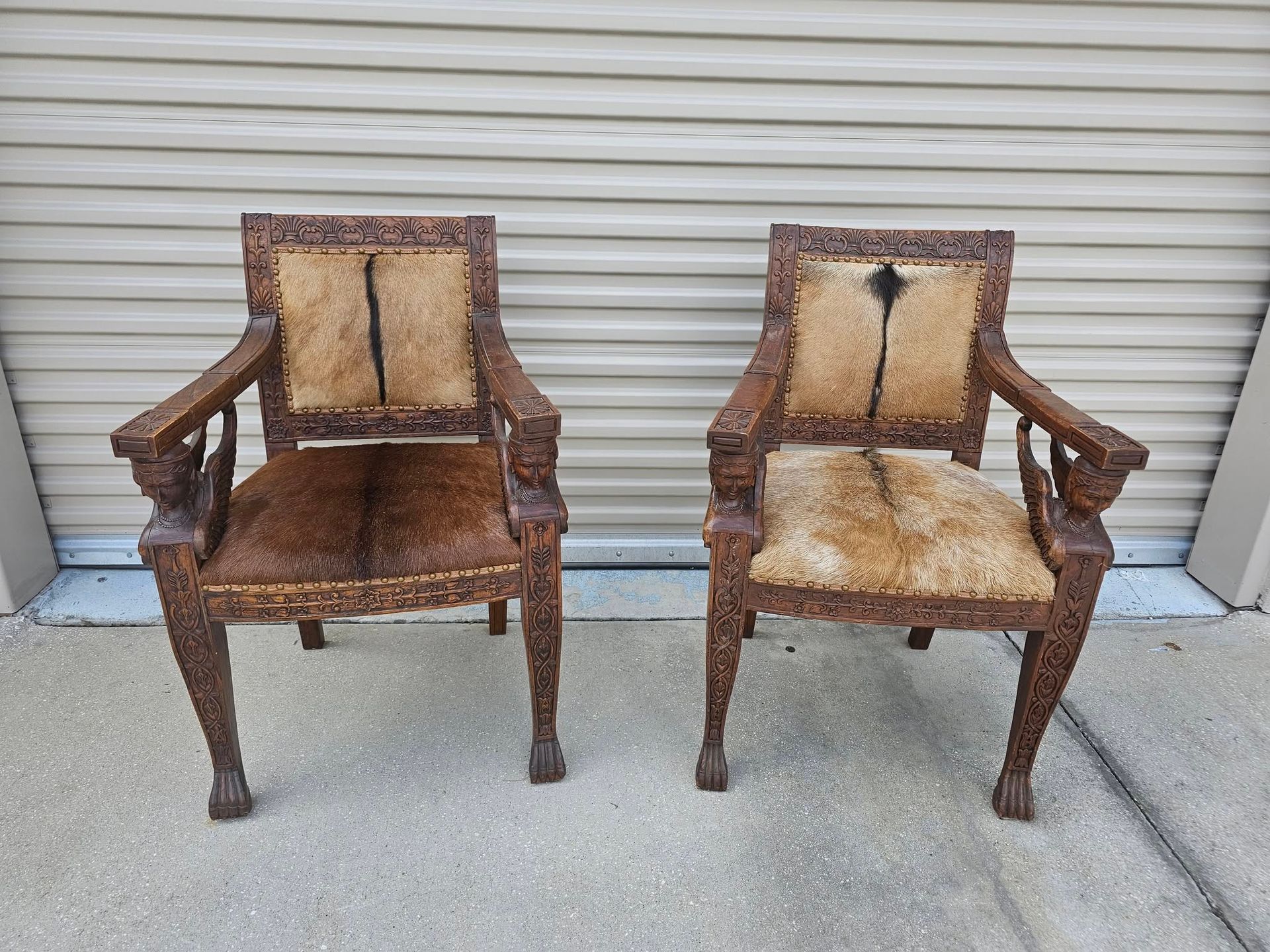 Two ornate wooden chairs with animal hide seats and backs; outdoor setting.