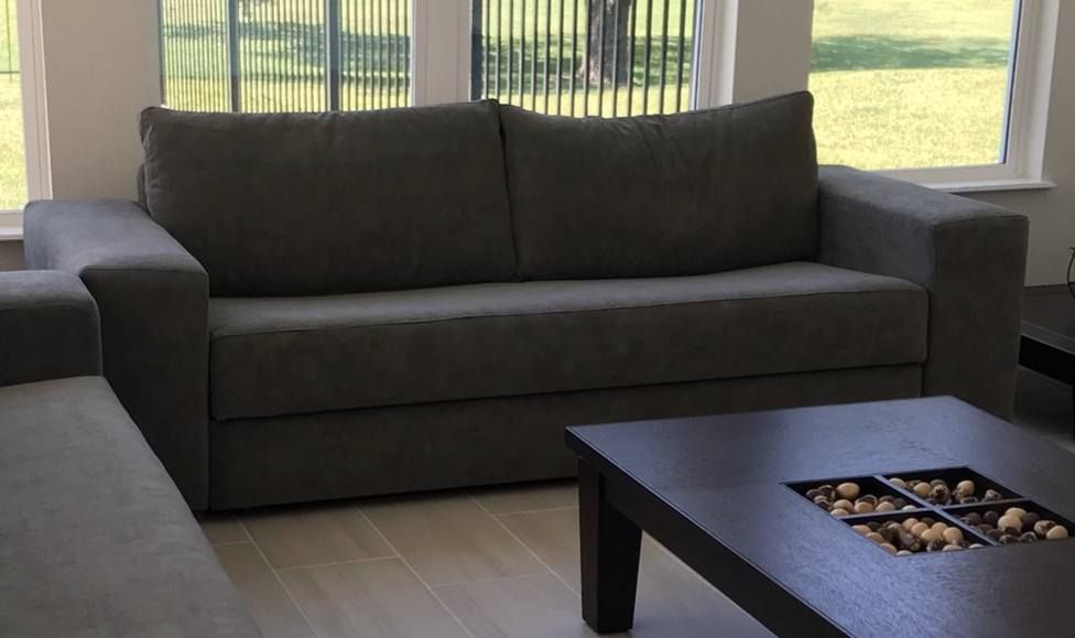 Gray sofa in a living room, with a dark square coffee table. Large windows in background.