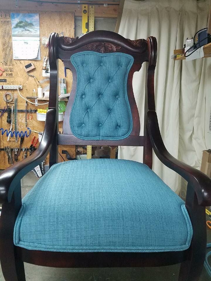 A restored antique wooden chair with teal fabric seat and backrest with button tufting, in a workshop.