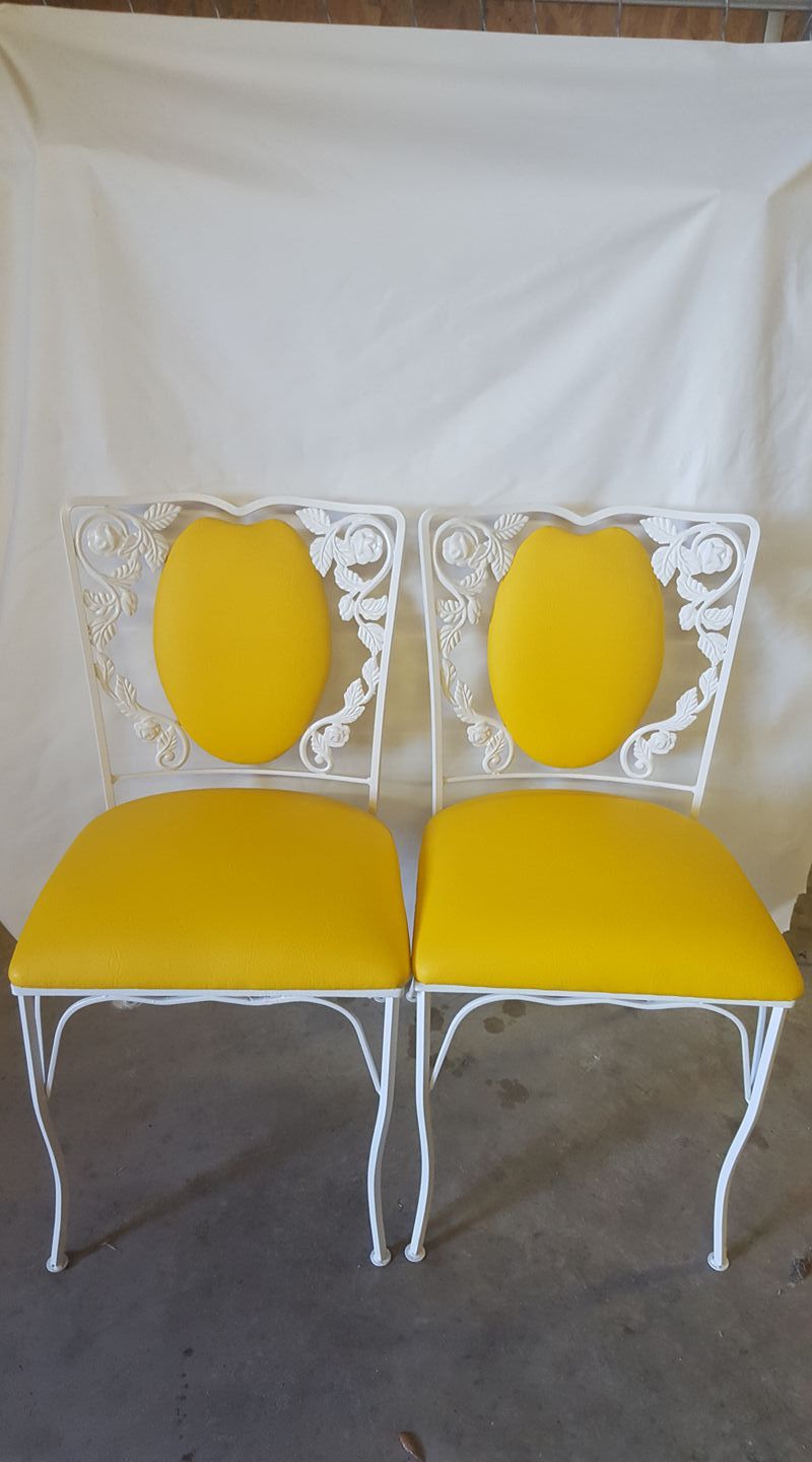 Two white wrought iron chairs with yellow cushions and backs.