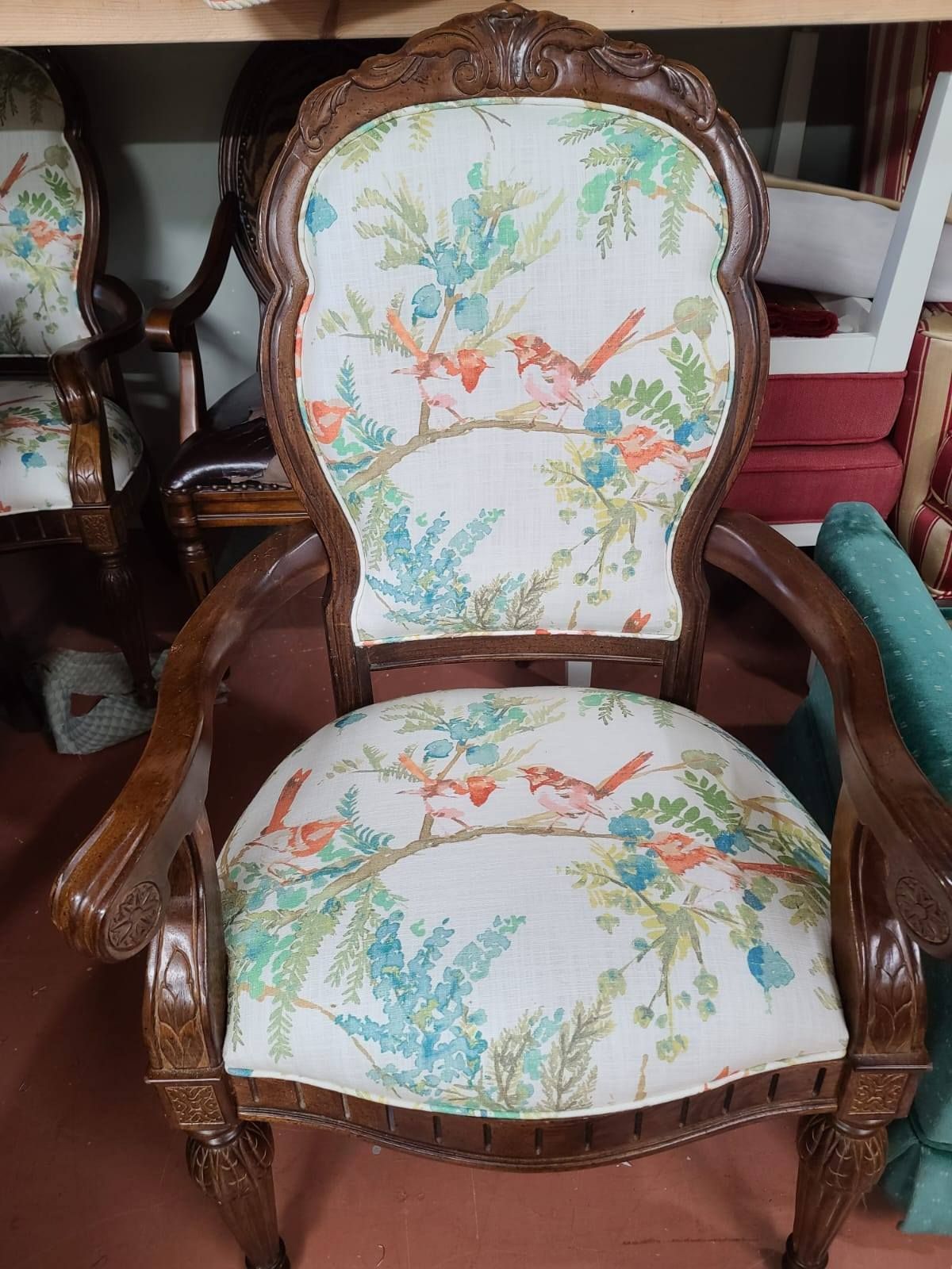 Ornate wooden armchair with bird-patterned fabric upholstery.