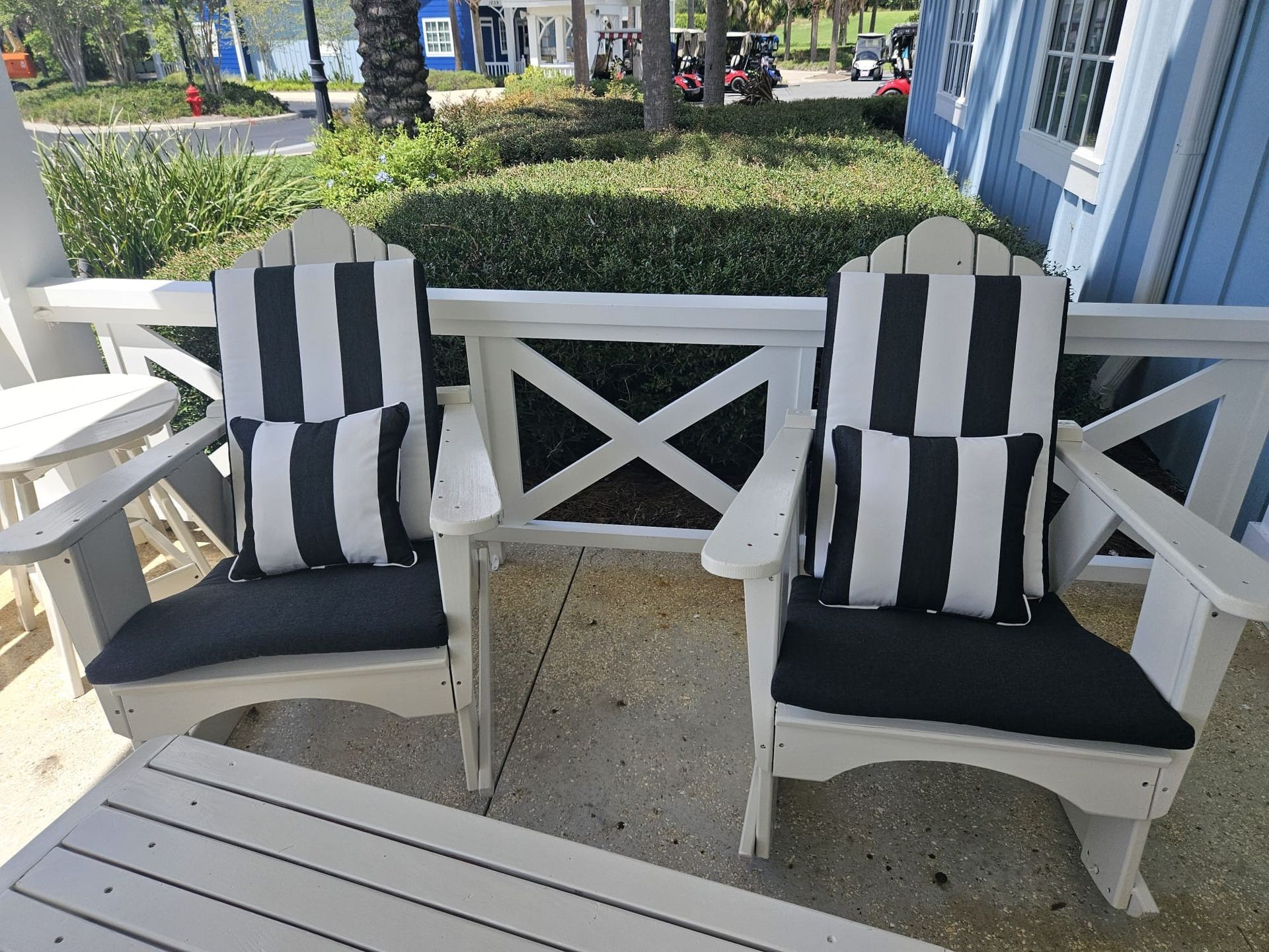 Two white chairs with black and white striped cushions on a porch.