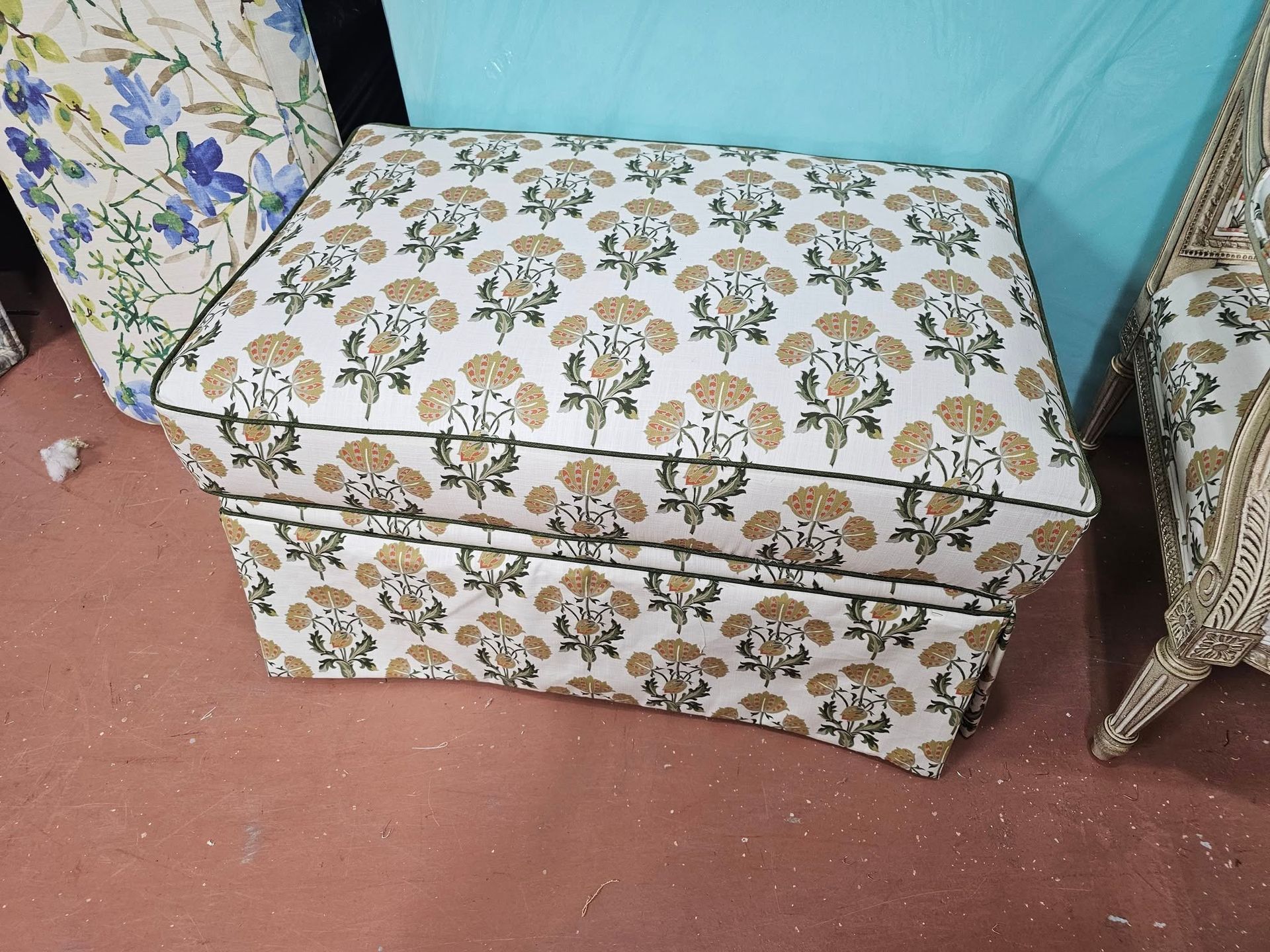 Upholstered ottoman with floral pattern on a red floor, part of a set.