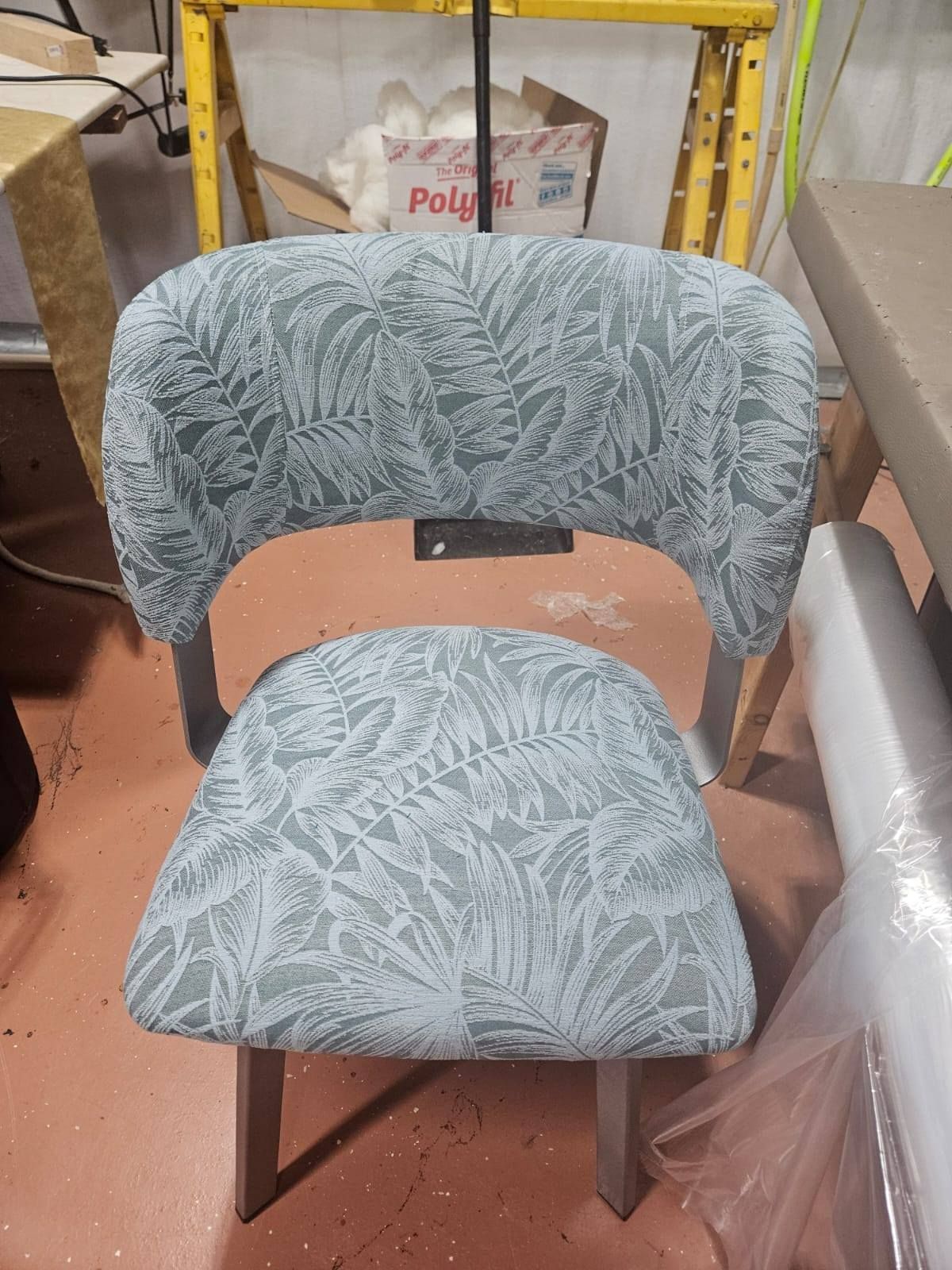 Upholstered chair with light green and white leaf pattern on light gray frame, workshop setting.