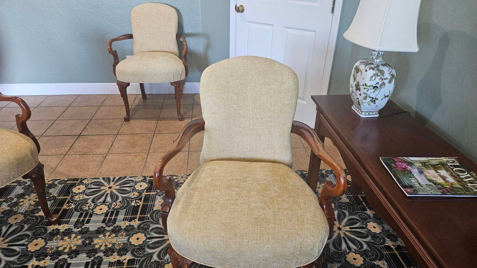 Three upholstered chairs in a room with a floral rug, table, and lamp.