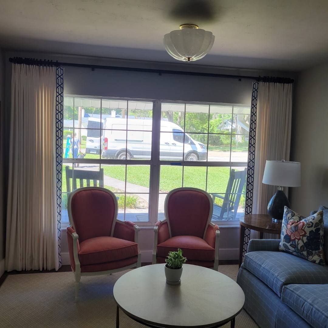 Living room with coral chairs, grey sofa, and large window with white drapes.