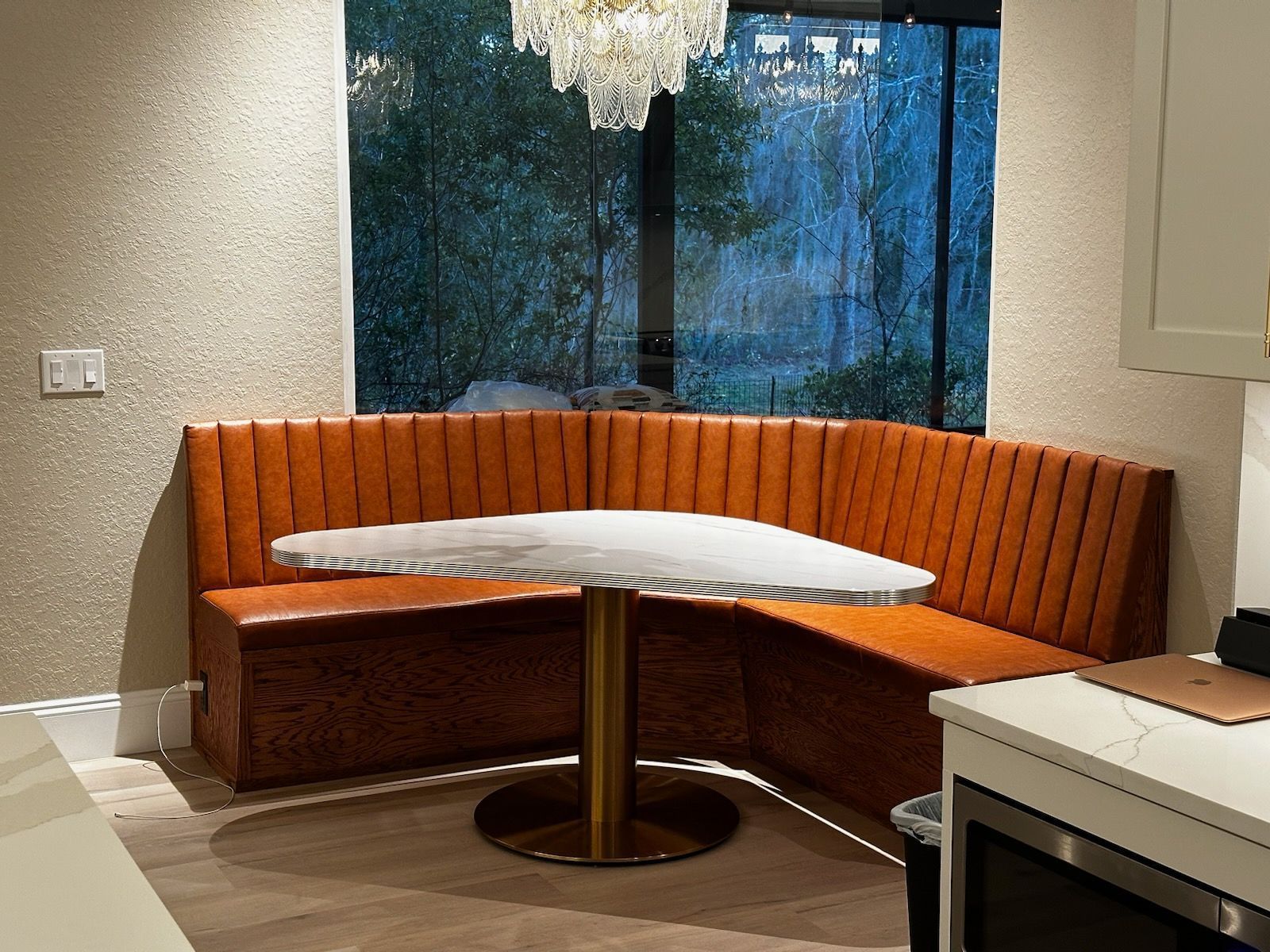 Orange booth seating in a kitchen corner with a round table and a view of a lush landscape.