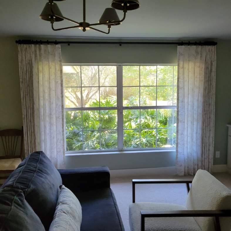 Living room with a large window, curtains, a sofa, and an armchair. Green walls and a chandelier are visible.