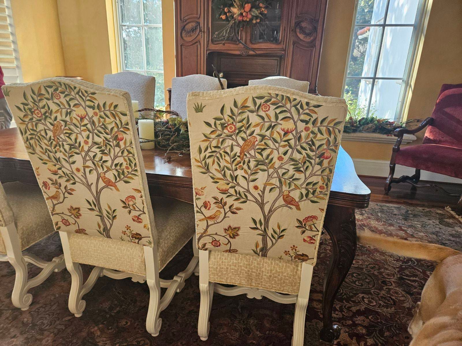 Two dining chairs with floral tapestry backs at a wooden table, in a sunlit dining room.