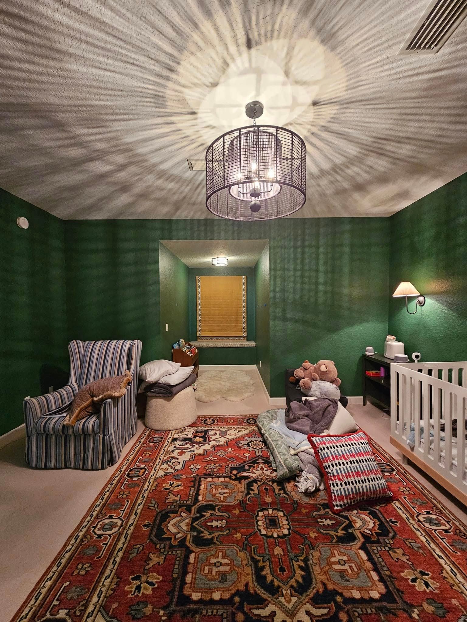 Green room with a patterned rug, patterned wall, and a crib.