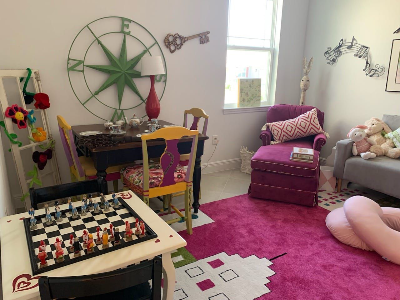 Child's room with chess set, desk, pink rug, armchair, and whimsical decor, including a compass rose.