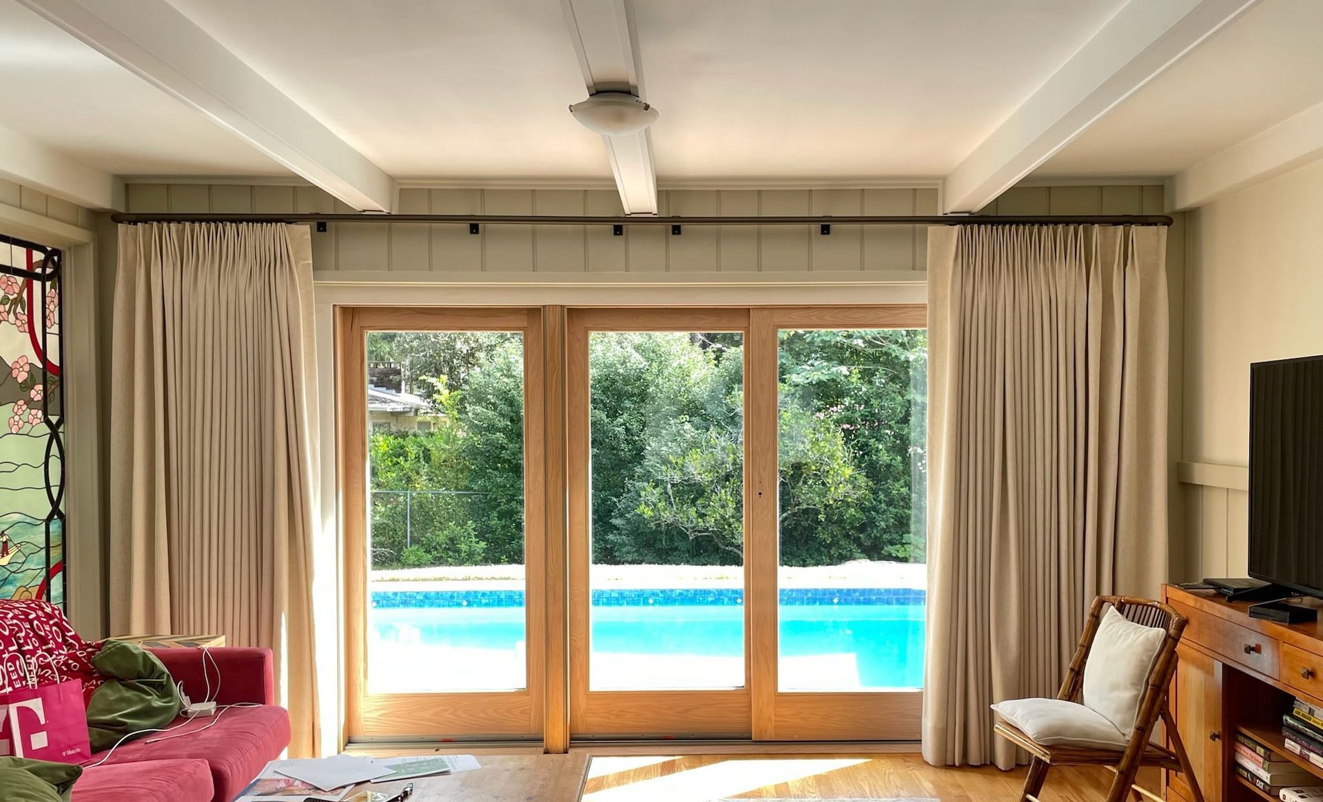 Living room with sliding glass doors overlooking a pool. Beige curtains frame the doors.