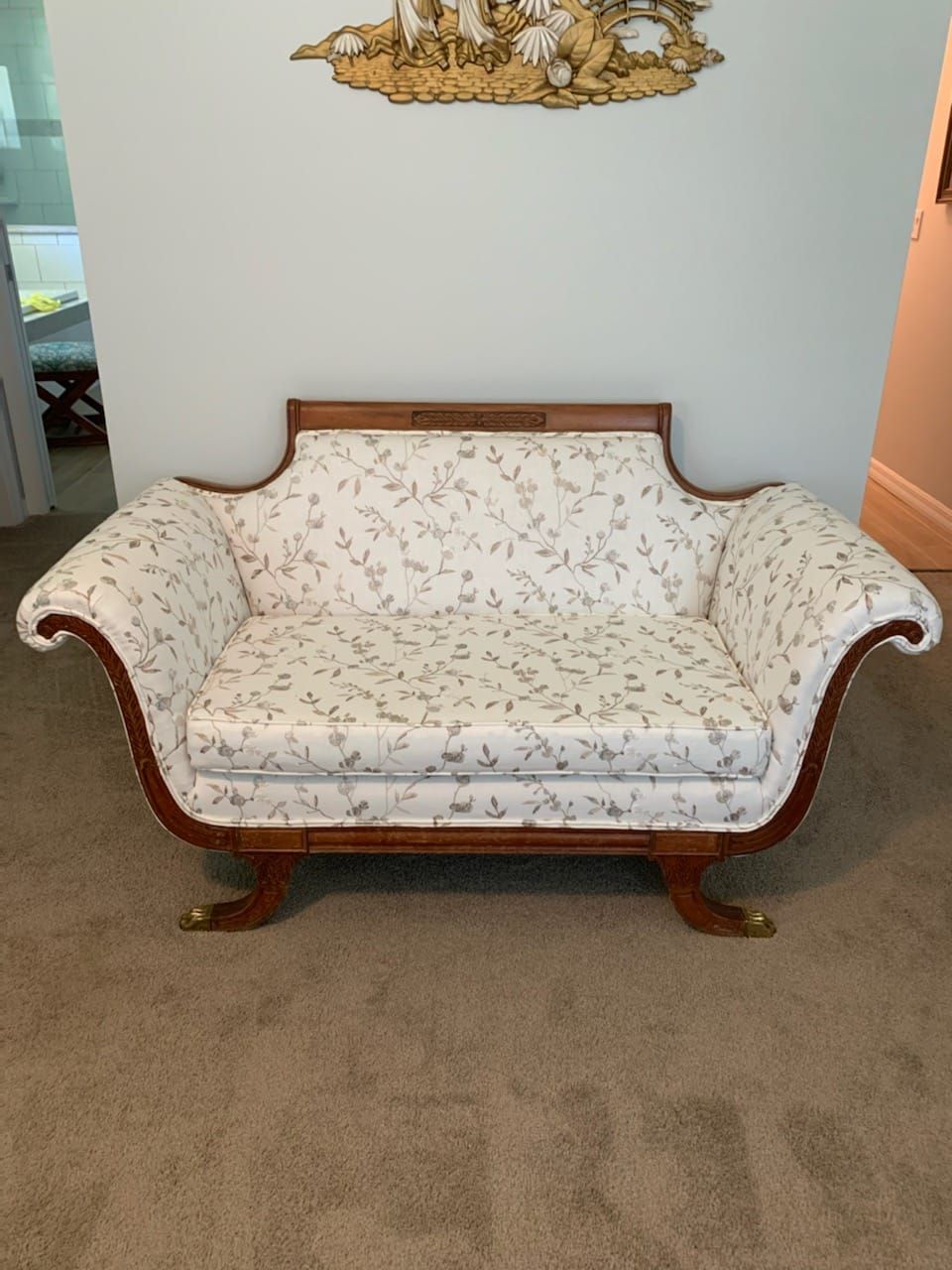 A vintage loveseat with light floral patterned cushions and a dark wooden frame, brass feet, in a home.