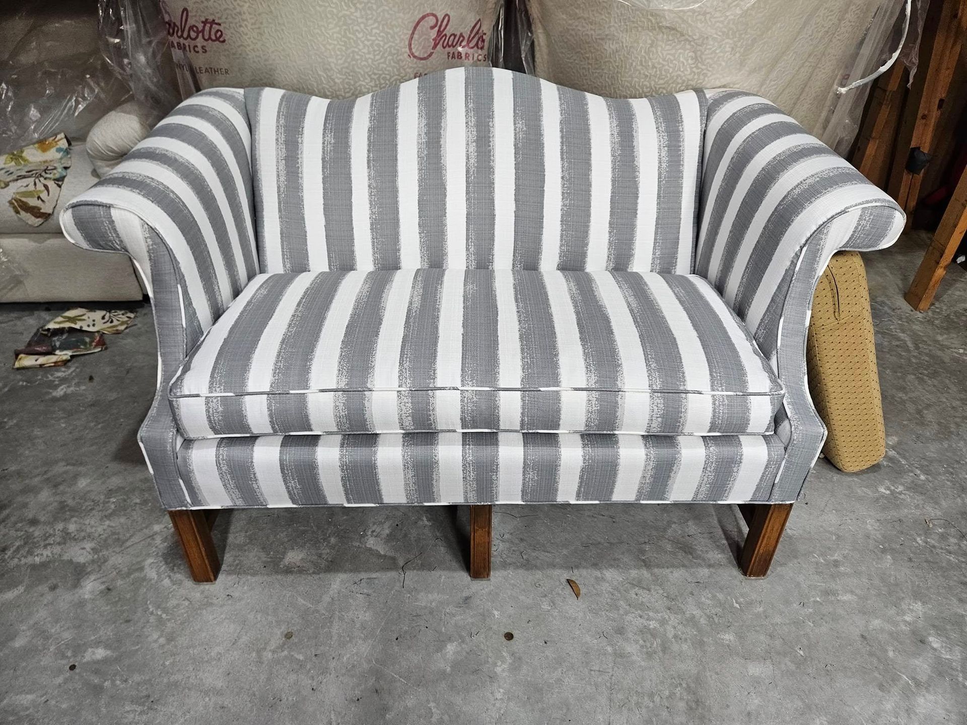 Gray and white striped loveseat on a gray floor; wooden legs and arms, indoor setting.