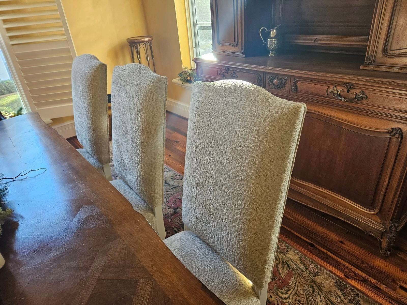 Three upholstered dining chairs sit at a long wooden table, with a large sideboard in the background.