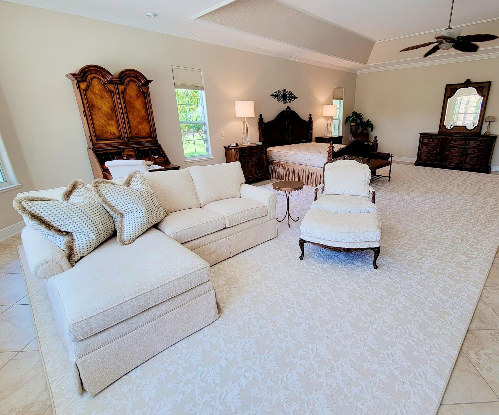 Spacious bedroom with cream sectional sofa, ornate bed, and white carpet.