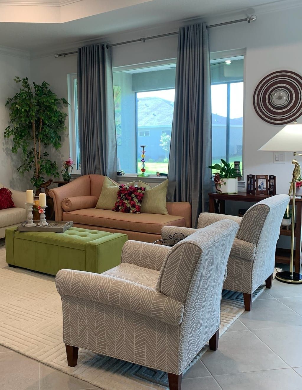 Living room: two patterned armchairs, a pink sofa, green ottoman, light gray curtains, and a view of a yard.