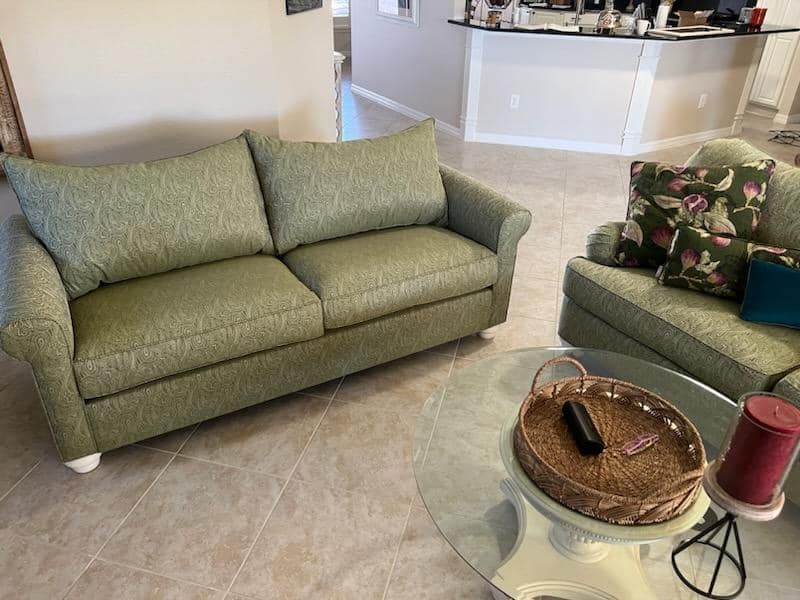 Green patterned couch and loveseat in a living room with a glass coffee table and tray.