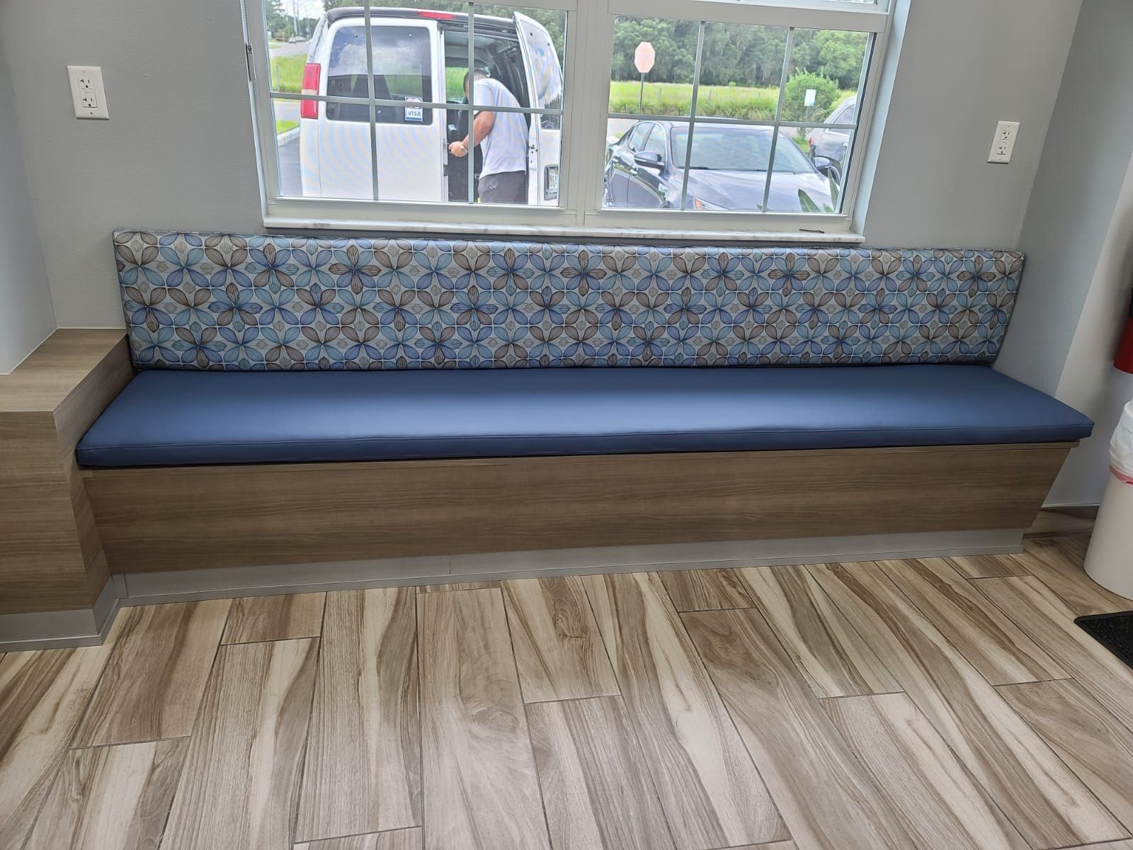 Built-in bench with blue cushions and patterned backrest, under a window in a room.