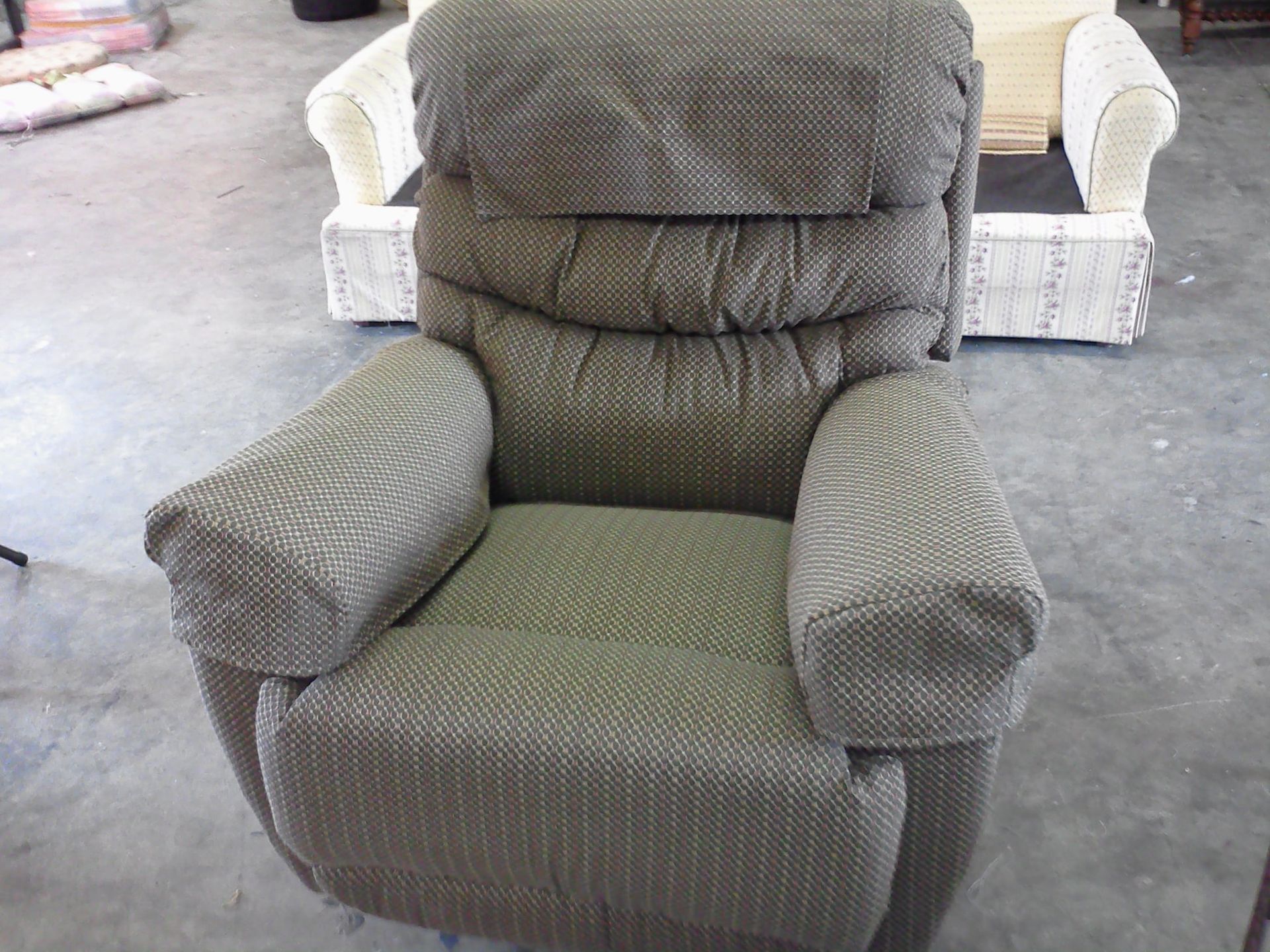A green patterned recliner chair, in a workshop setting, with a sofa in the background.