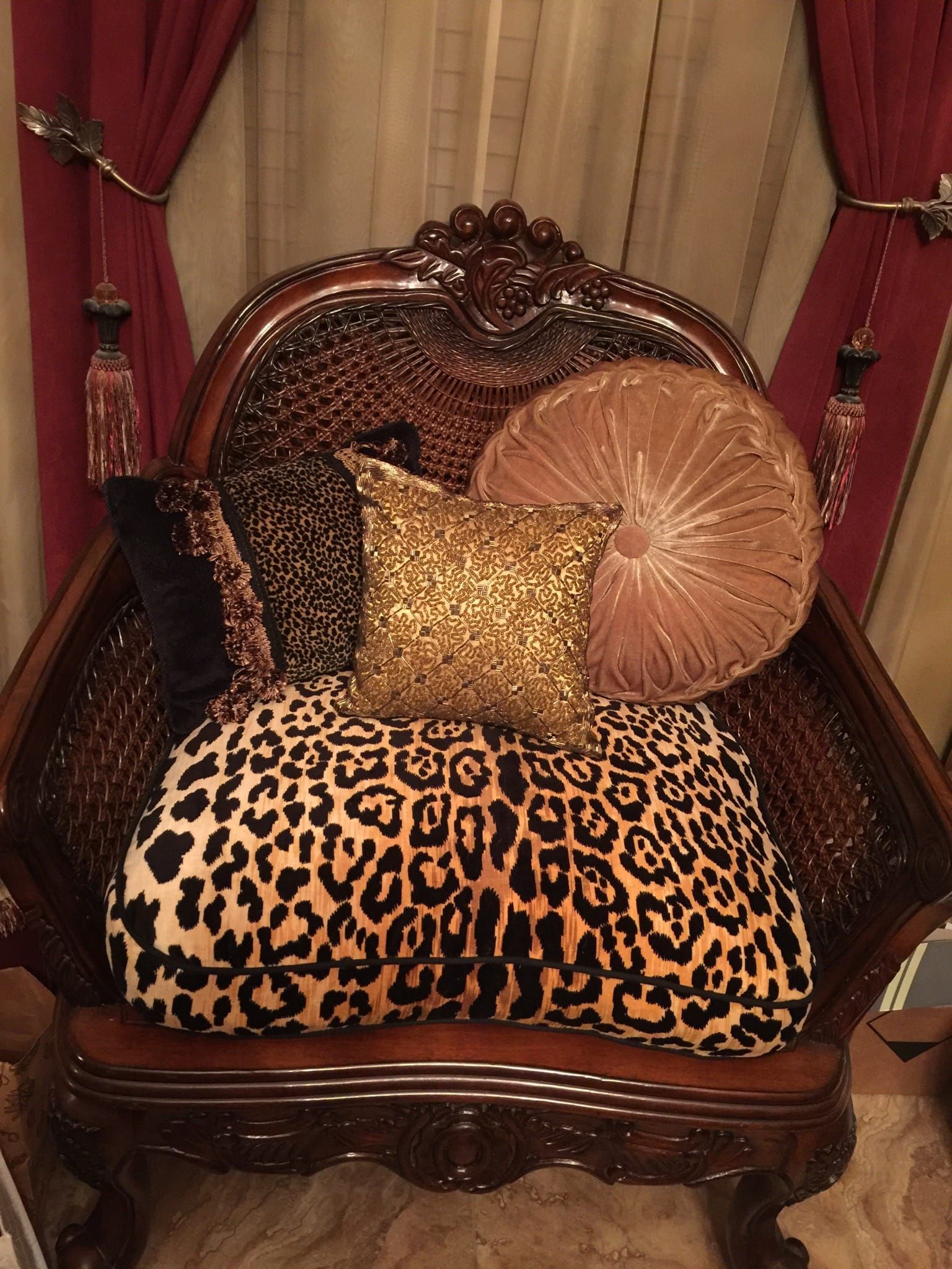 Ornate wooden chair with leopard print and gold pillows. Red curtains in the background.