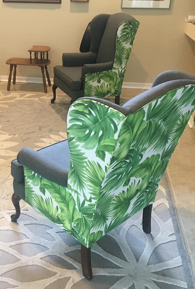 Two wingback chairs with tropical leaf pattern backs, gray sides, on a patterned rug.