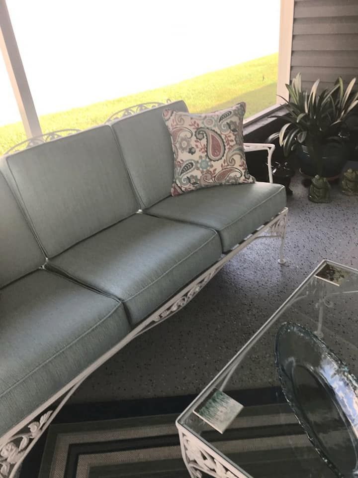 A light blue cushioned outdoor couch with a patterned pillow, on a patio.