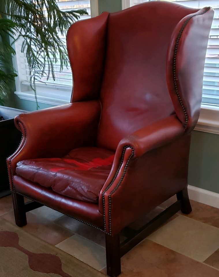 Red leather wingback chair in a room with a window, the seat shows wear.