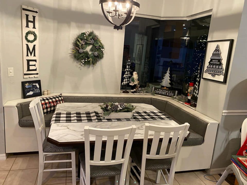 A festive dining area: gray bench seating, a marble table, and white chairs. Holiday decorations adorn the space.