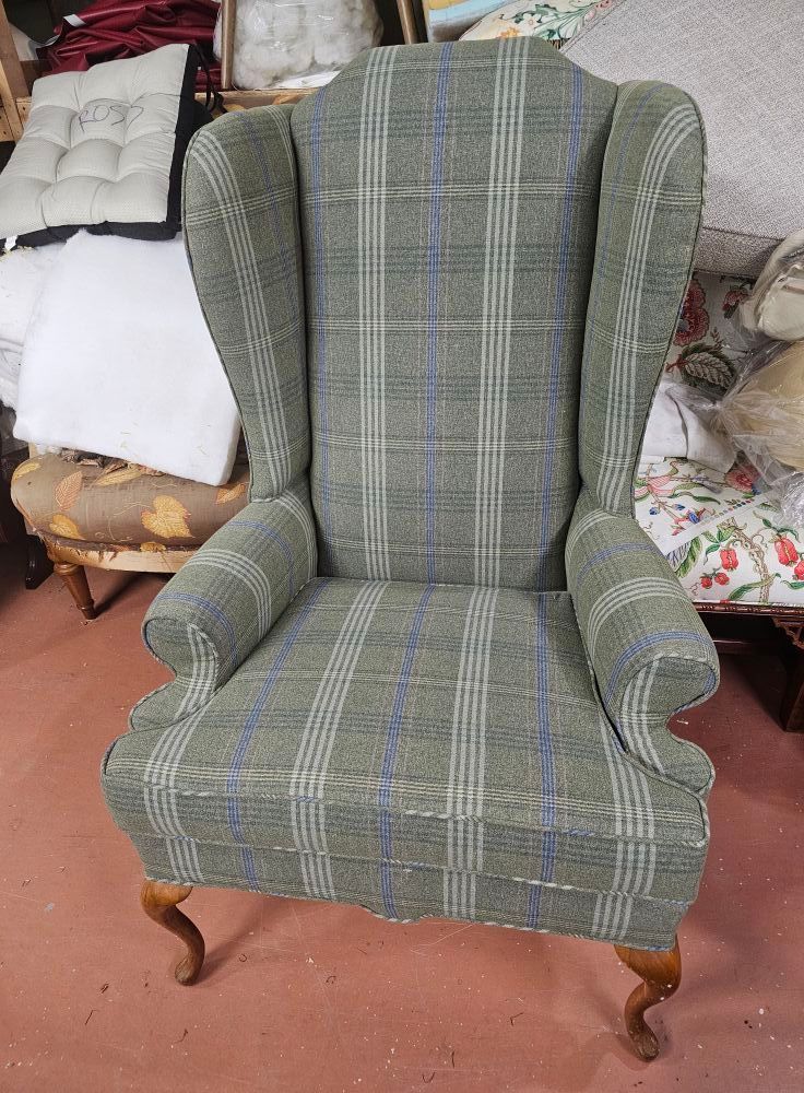 Wingback armchair with green plaid fabric, wooden legs, set in a room with other furniture.