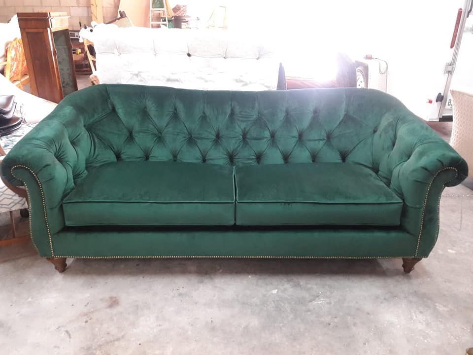Green velvet Chesterfield sofa with button tufting, set in a workshop.
