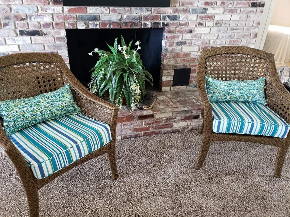Two wicker chairs with blue striped cushions and decorative pillows sit in front of a brick fireplace.