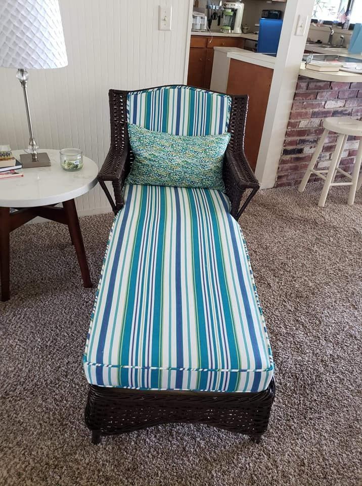Wicker chaise lounge with striped blue and green cushion, teal pillow, next to a side table.