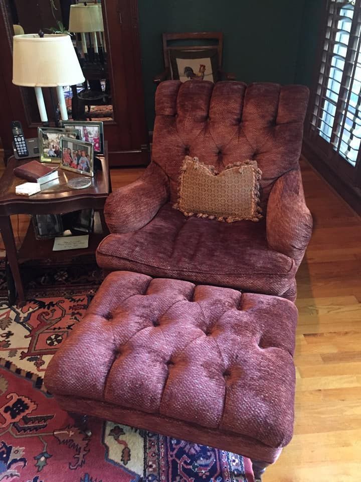 Red tufted armchair and ottoman with a small woven pillow, beside a small table with lamp.