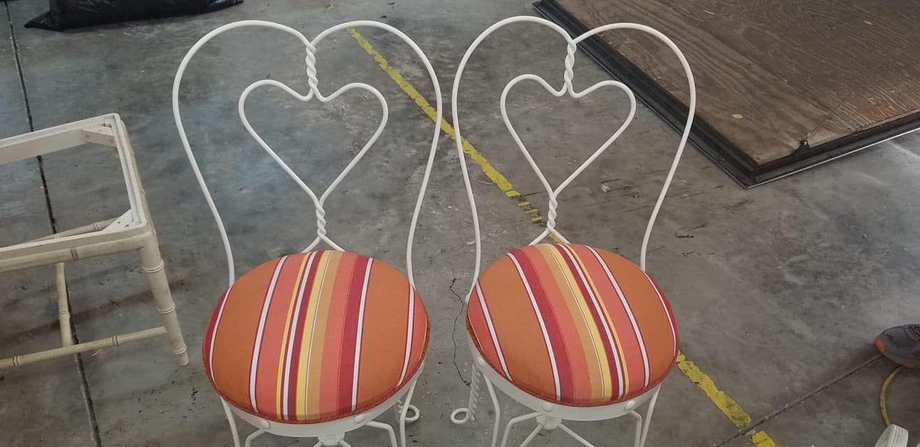 Two white metal chairs with heart-shaped backs and striped orange cushions.