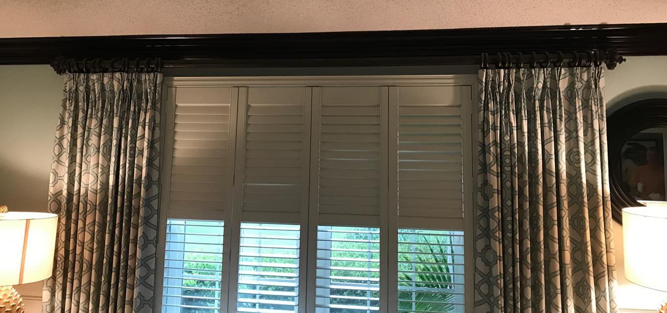 Window with white shutters, surrounded by patterned curtains. The window is set in a room with a dark-colored trim.