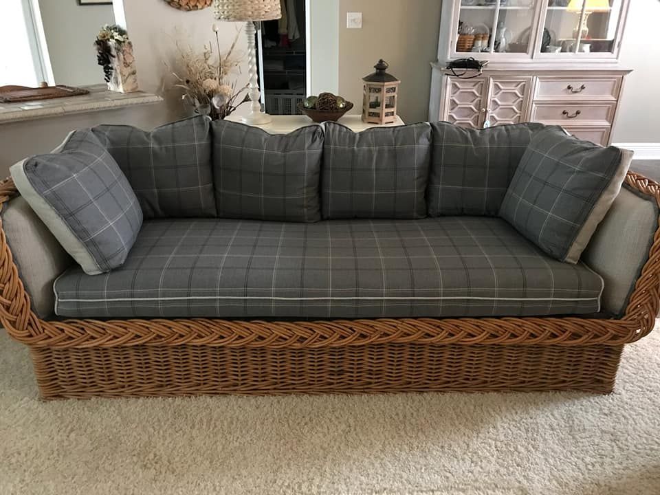 Wicker sofa with gray plaid cushions, two throw pillows, and white trim on a beige carpet.