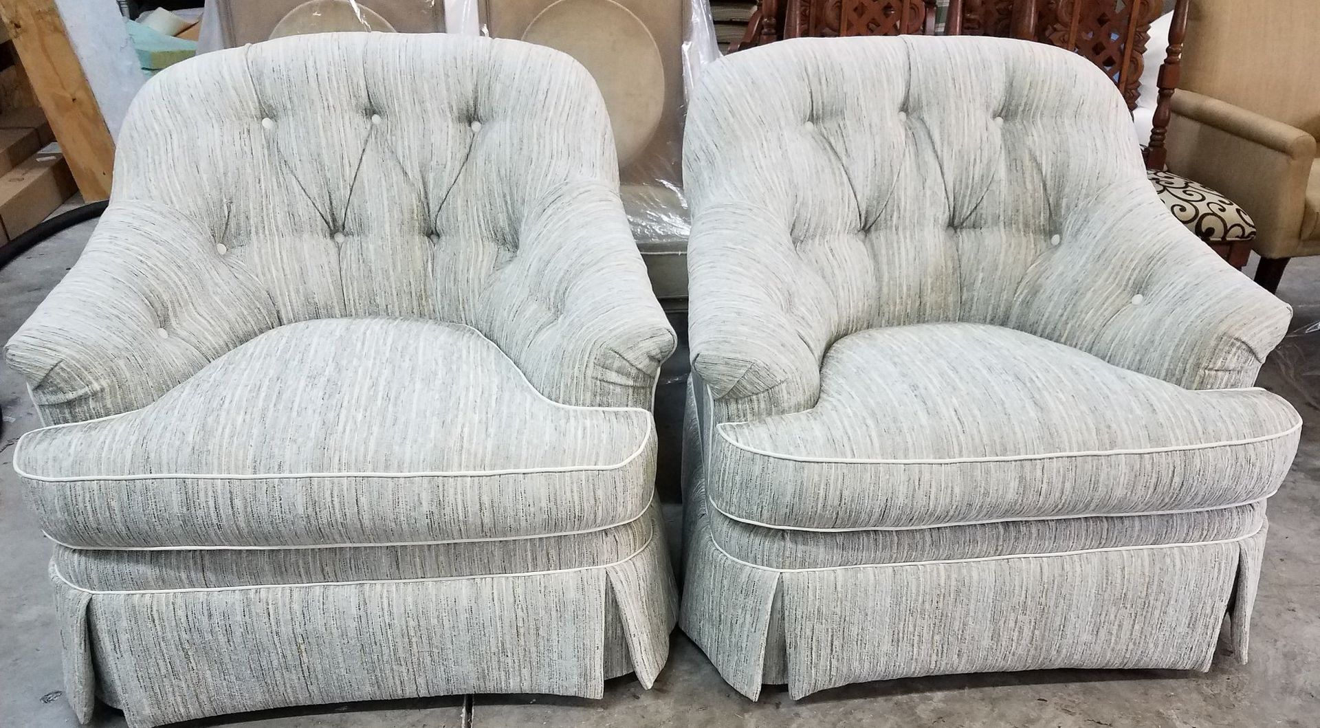 Two matching light-colored armchairs with buttoned backs and skirted bases.