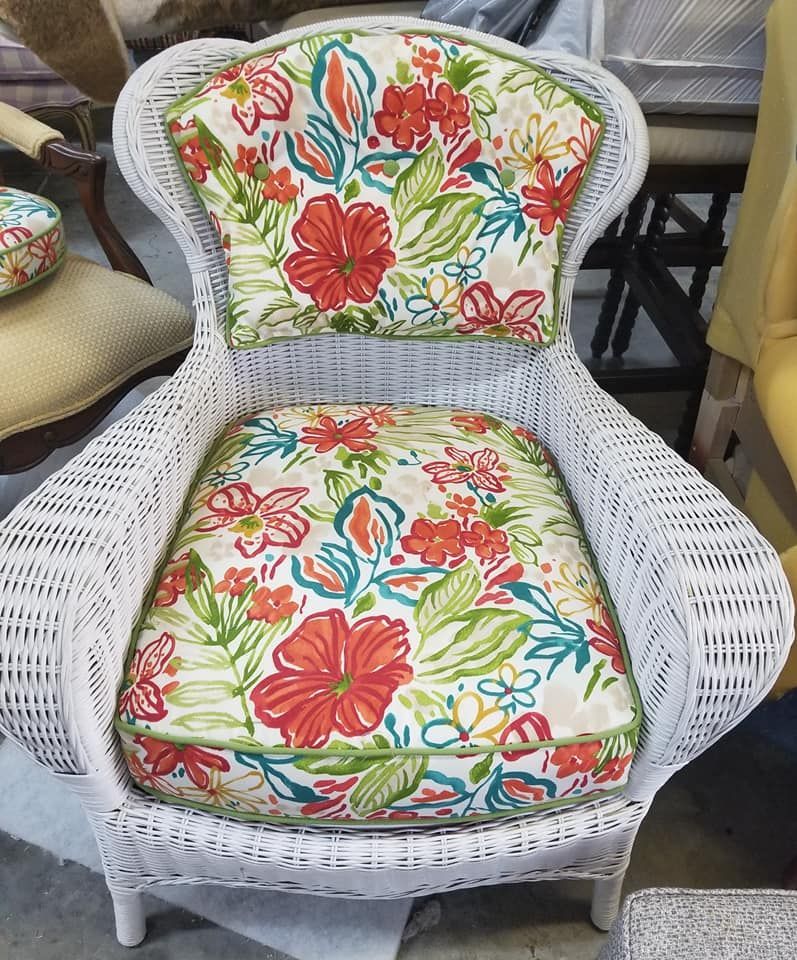 White wicker chair with floral cushions: red hibiscus flowers, green leaves.