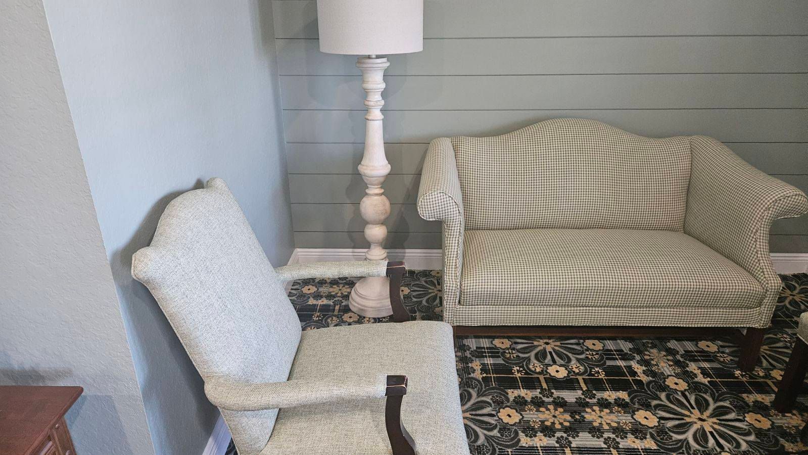 An ornate floor lamp stands between two upholstered chairs in a room with patterned wallpaper.
