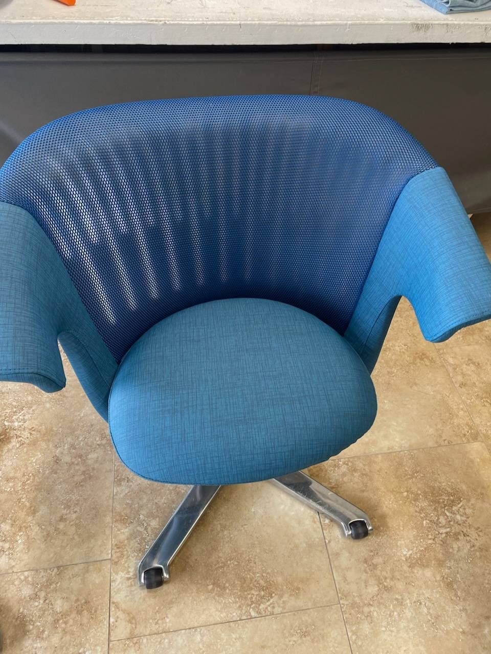 Blue office chair with a mesh back and padded seat on a silver base, set on a tiled floor.