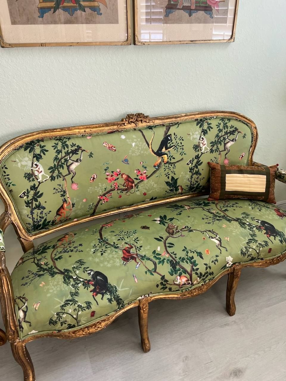 Green, floral patterned antique settee with gold trim, small framed artwork displayed on the seat.