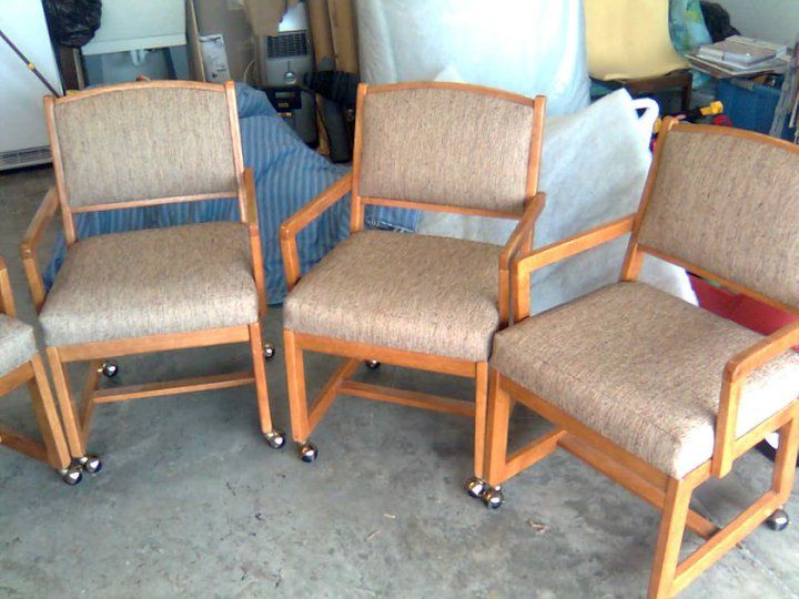 Three wooden armchairs with beige patterned upholstery and casters on a concrete surface.