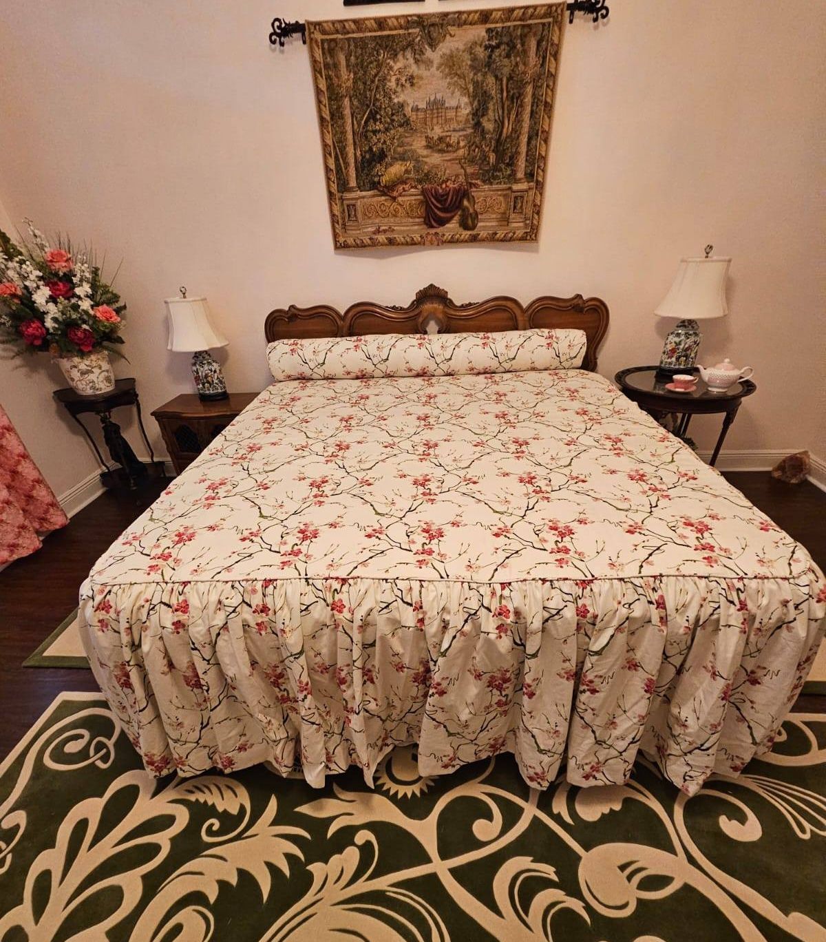 Bedroom with floral bedding, a decorative tapestry above the wooden headboard, and lamps on the bedside tables, set on a patterned rug.