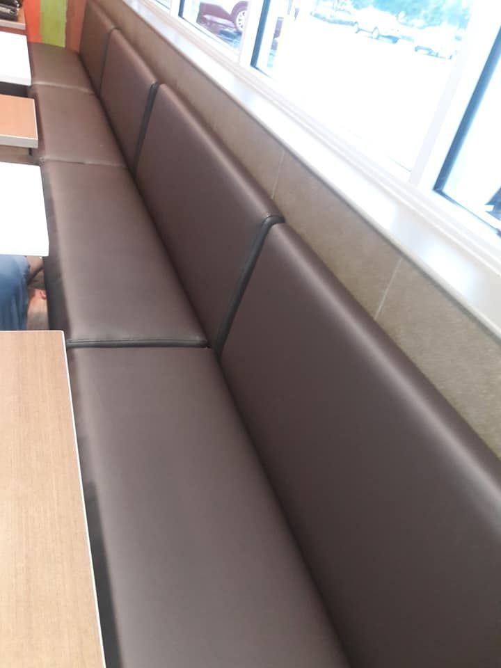 Brown leather booth seating in a restaurant next to a window and small tables, likely for customers.