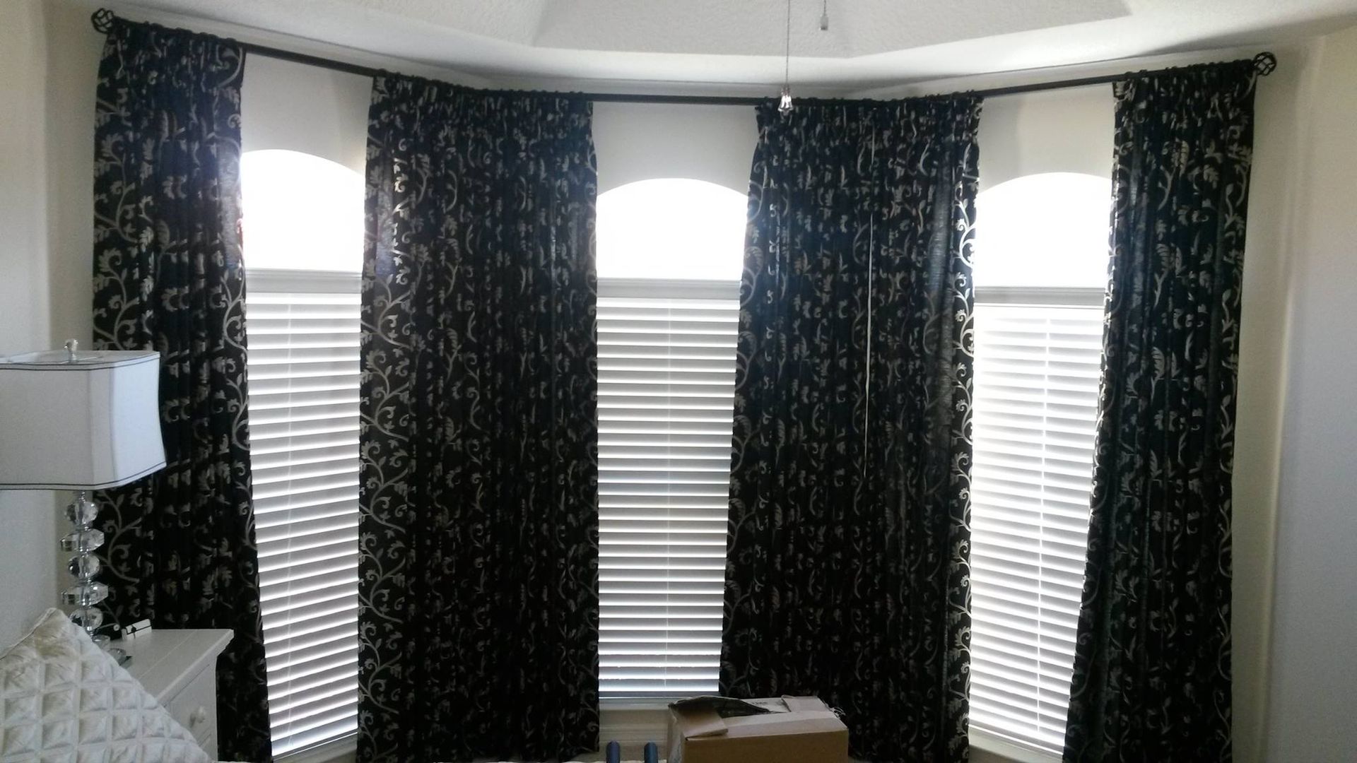 A window with dark patterned curtains and white blinds. It's in a room with a curved ceiling.