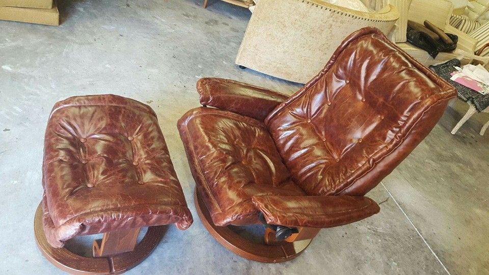 Brown leather recliner chair and matching ottoman on a wooden base. The chair is tilted back, showing button-tufted cushions.