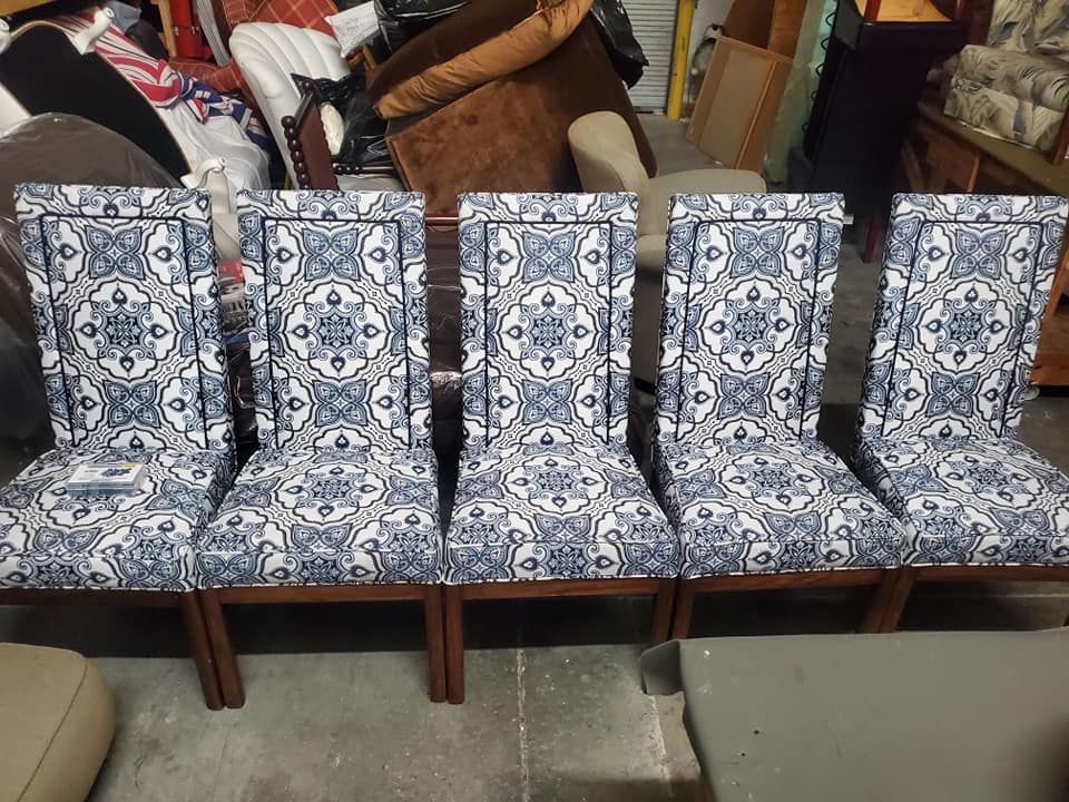 Five dining chairs with blue and white patterned upholstery and wooden frames are lined up in a room.
