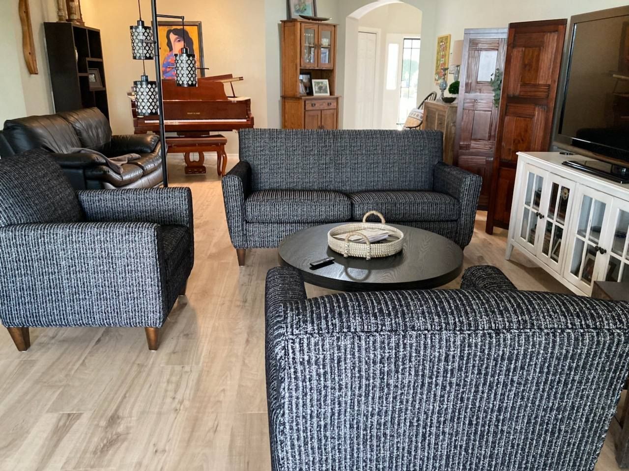 Living room with gray patterned furniture, a round coffee table, and a piano in the background.