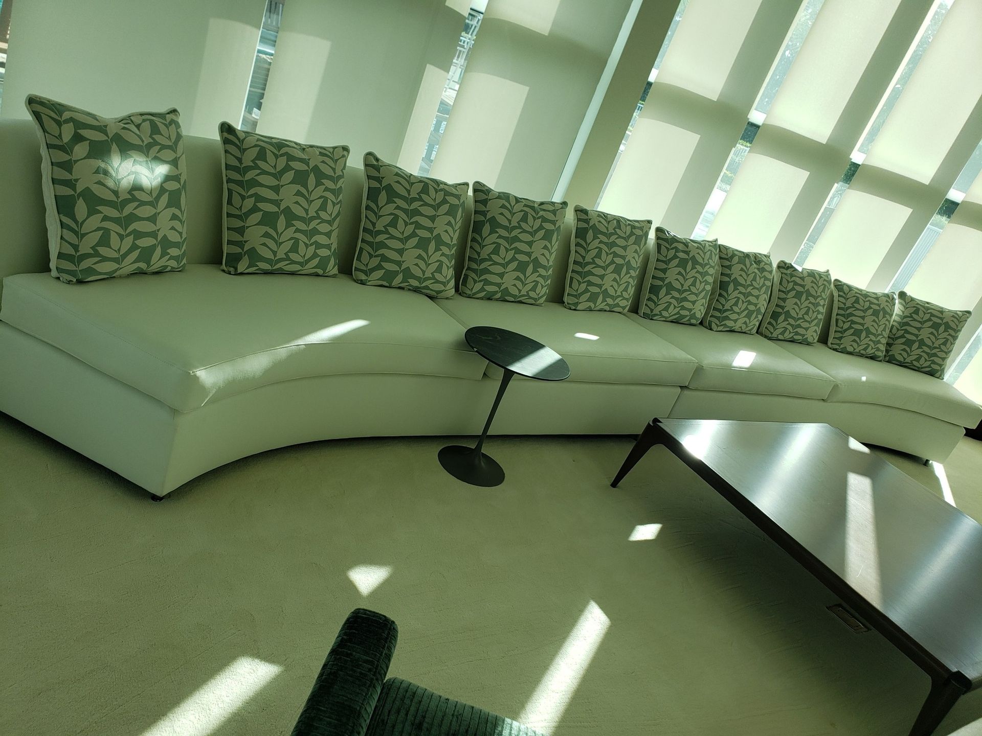 A curved white couch with patterned pillows in a brightly lit modern room. A small black side table and a dark square coffee table are nearby.